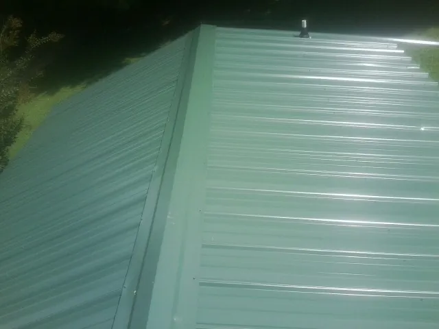 New green metal panels meeting at the ridge of a roof — Flat Roof Repair work by our crew in Maineville