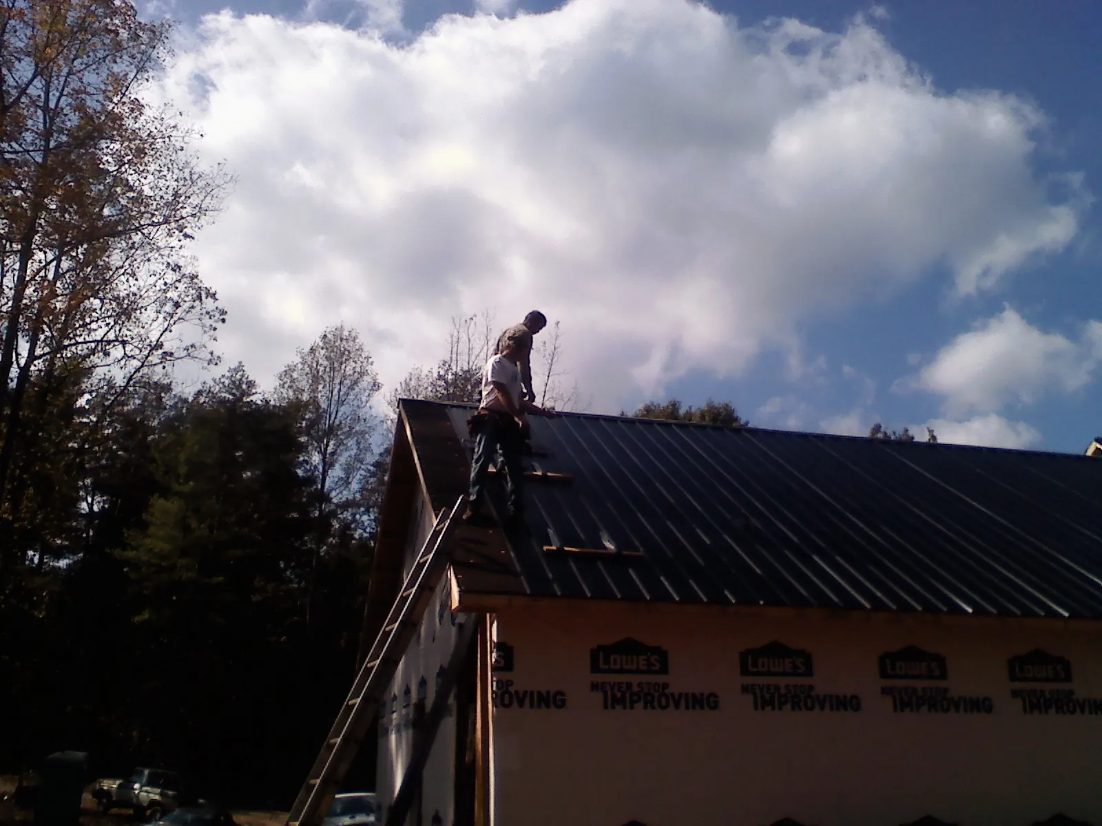 Roofer fastening dark metal panels high against a cloudy sky, from a Roof Inspection job in Maineville