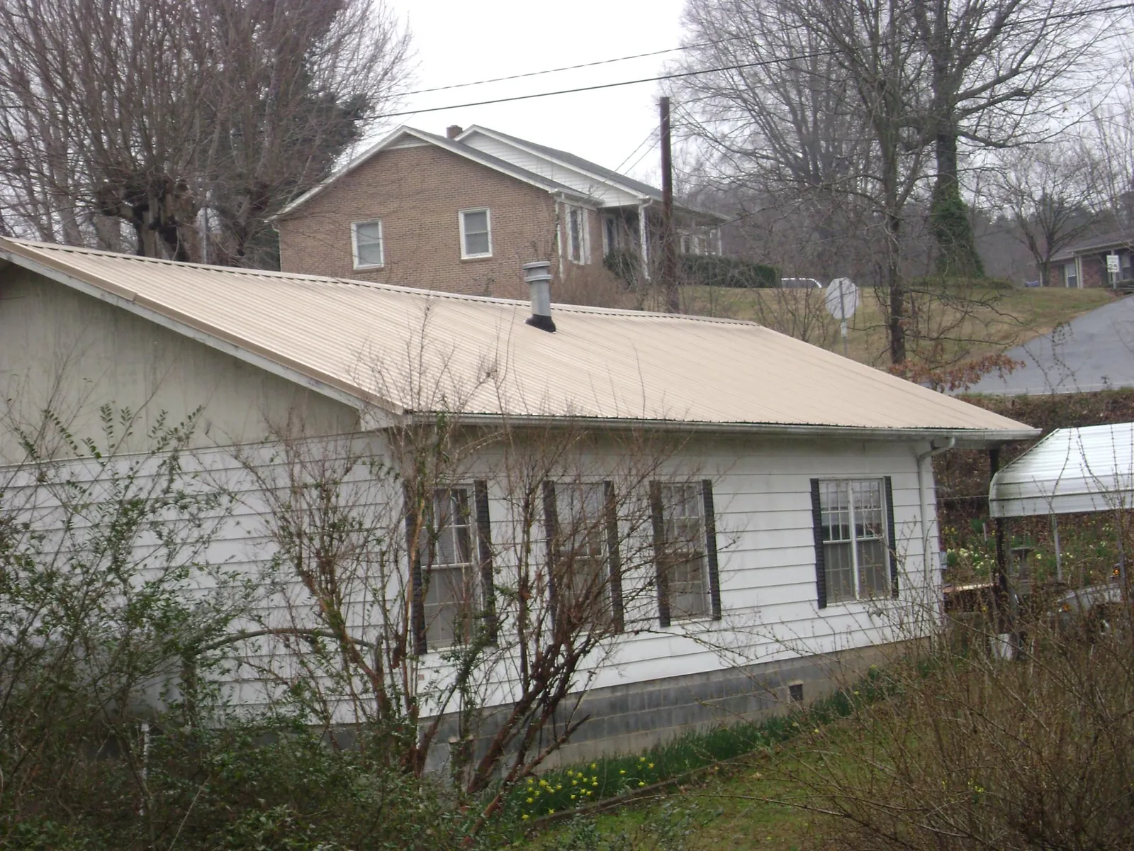 Tan metal roof on a white sided house set into a hillside — Commercial Roofing by Roofing Brothers in Maineville